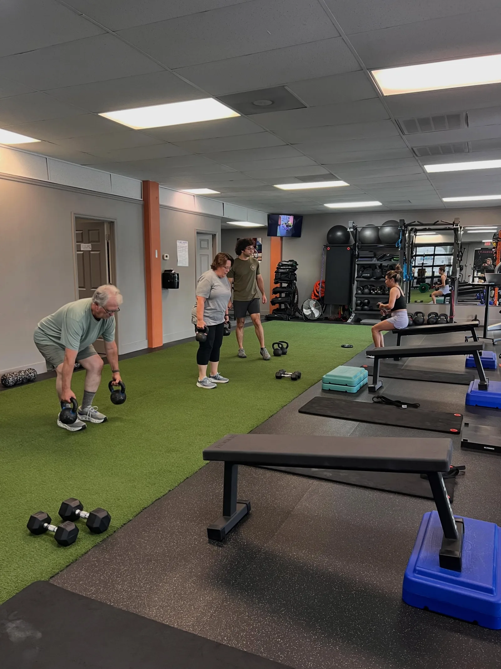 A coach guiding members through a kettlebell session on the turf